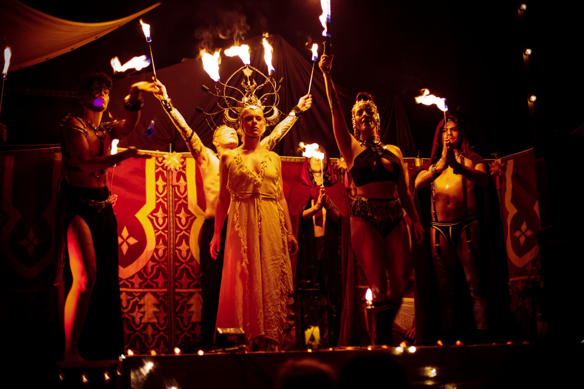 Performers holding flames before red patterned textiles
